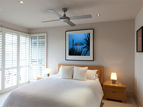 Neutral holiday home bedroom wooden bedhead and textured blanket with lamp and ceiling fan